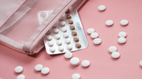 Pink background with birth control pills spilling out of a bag