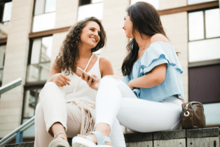 Two women smiling at each other and holding a phone in one hand