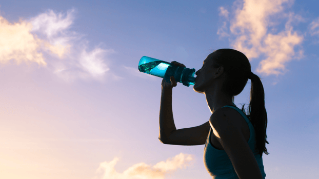 Woman drinking water with a sunset behind her Woman drinking water with a sunset behind her
