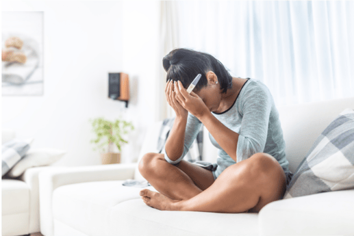 Devastated woman sitting on a couch with hands overhead, holding a pregnancy test 