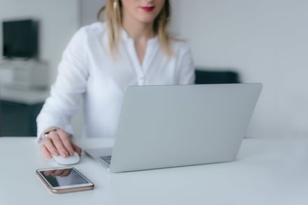 Women siting at a white desk with computer open and hand on mouse